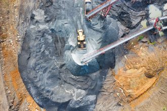 Vista aérea de uma grande área de mineração industrial, com máquinas pesadas e correias transportadoras em operação.